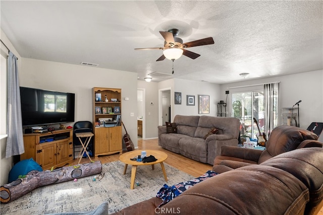 living room with light hardwood / wood-style flooring, a textured ceiling, and ceiling fan