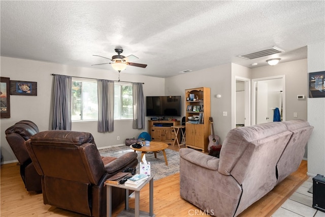 living room featuring a textured ceiling, light wood-type flooring, and ceiling fan