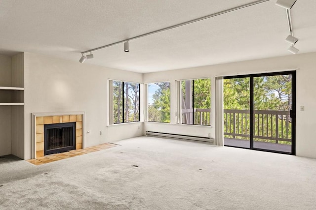 unfurnished living room featuring carpet, baseboard heating, a tiled fireplace, and rail lighting