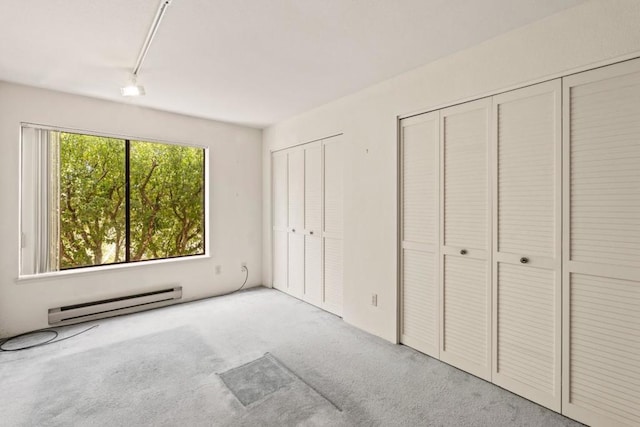 unfurnished bedroom featuring a baseboard heating unit, two closets, and light carpet