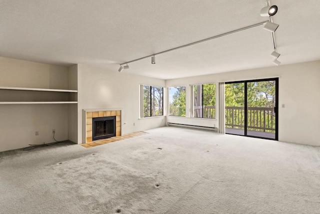 unfurnished living room featuring carpet flooring, rail lighting, a fireplace, and a baseboard radiator