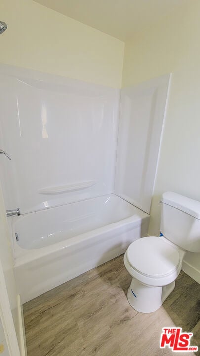 bathroom with toilet,  shower combination, and wood-type flooring