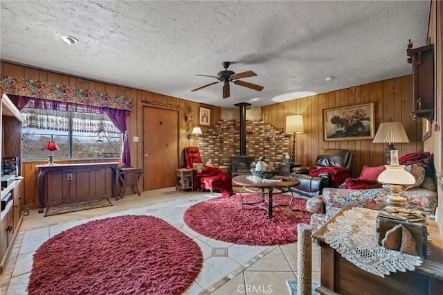 tiled living room featuring ceiling fan, a wood stove, a textured ceiling, and wood walls