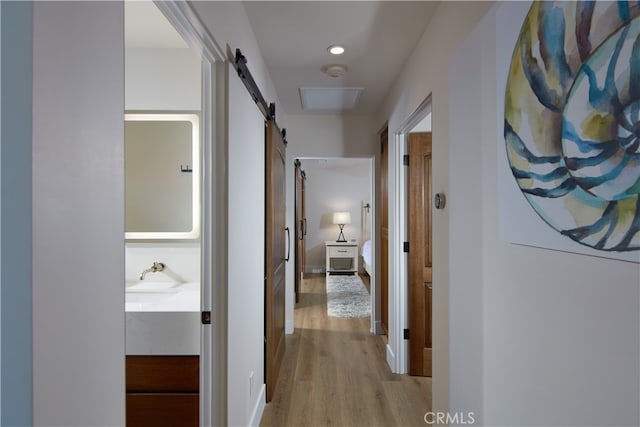 corridor with sink, a barn door, and light wood-type flooring