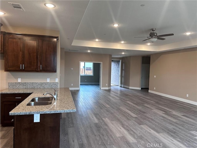 kitchen with ceiling fan, sink, dark wood-type flooring, a raised ceiling, and light stone counters