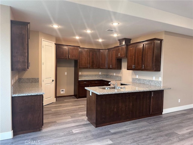 kitchen featuring dark brown cabinets, light stone countertops, kitchen peninsula, and light hardwood / wood-style flooring