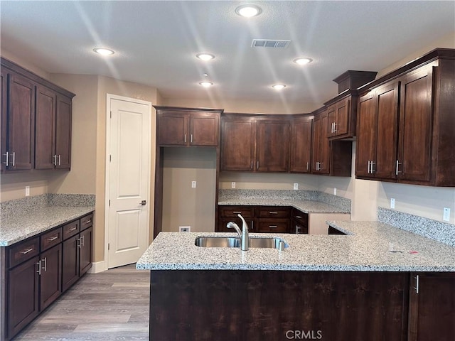 kitchen featuring dark brown cabinetry, light stone countertops, sink, kitchen peninsula, and light hardwood / wood-style floors