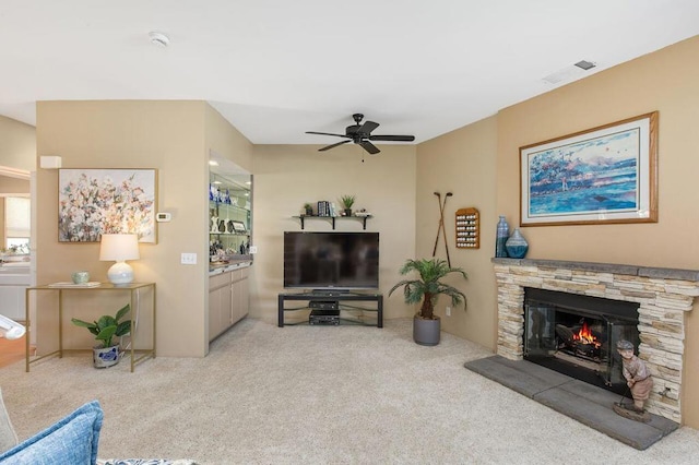 living room featuring a stone fireplace, ceiling fan, and light colored carpet