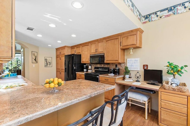 kitchen featuring a kitchen bar, light wood-type flooring, kitchen peninsula, and black appliances