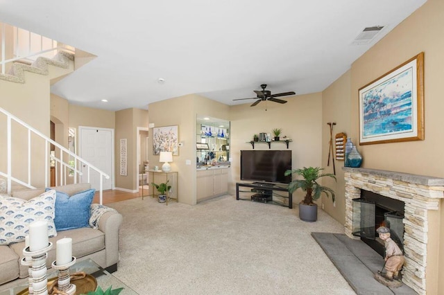 carpeted living room featuring a stone fireplace and ceiling fan