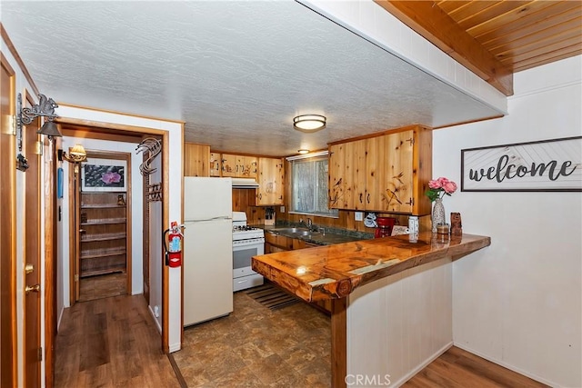 kitchen with white appliances, dark wood-type flooring, sink, wooden walls, and kitchen peninsula