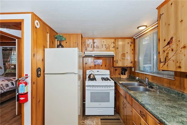 kitchen with white appliances, sink, wooden walls, a textured ceiling, and light hardwood / wood-style floors