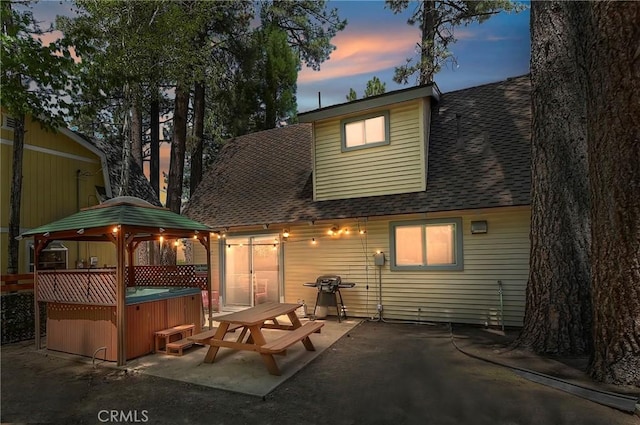 back house at dusk featuring a gazebo, a patio area, and a hot tub