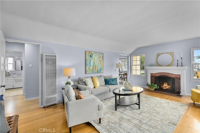 living room featuring a brick fireplace, lofted ceiling, and light hardwood / wood-style flooring