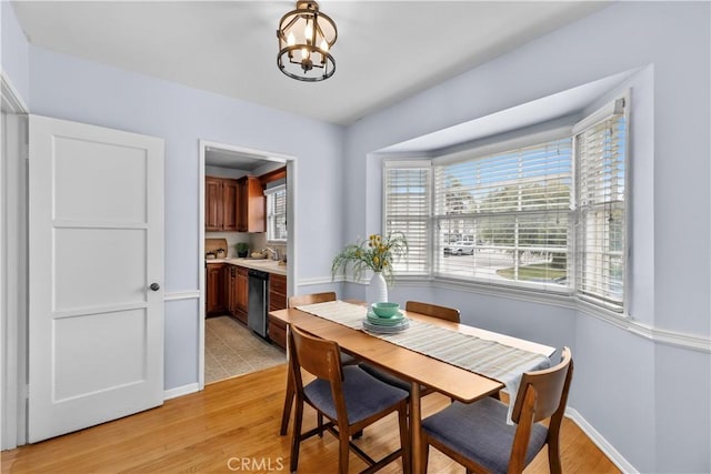 dining area featuring sink, light hardwood / wood-style floors, a healthy amount of sunlight, and a notable chandelier