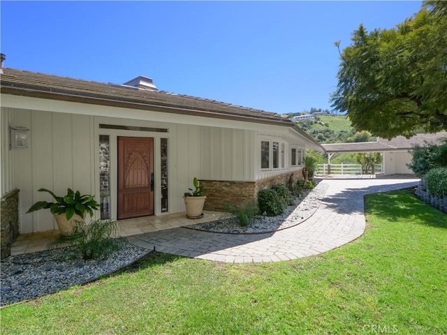 view of exterior entry featuring a lawn and a carport