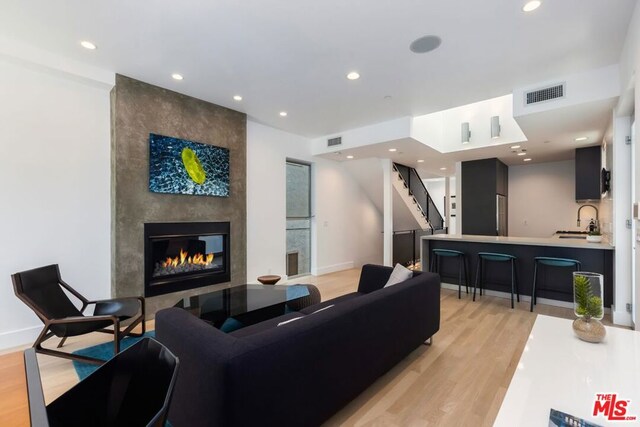 living room with light wood-type flooring, a large fireplace, and sink