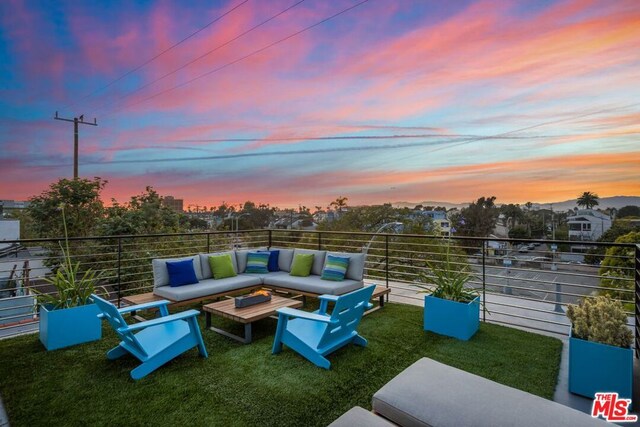 patio terrace at dusk with a balcony, a yard, and an outdoor living space