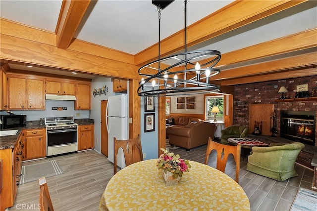 dining space with a brick fireplace, a chandelier, beam ceiling, and light wood-type flooring