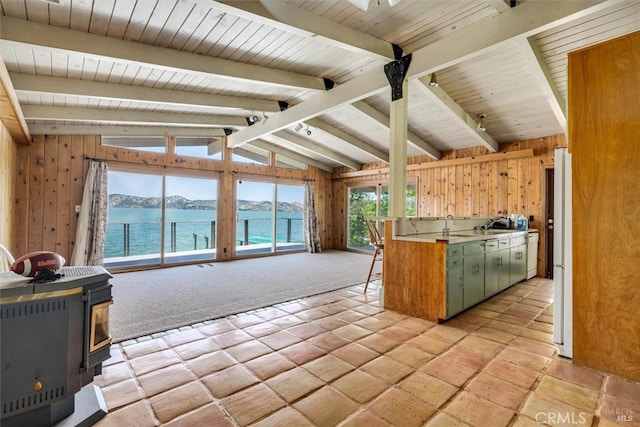 kitchen featuring vaulted ceiling with beams, wooden walls, a wood stove, green cabinetry, and a water view