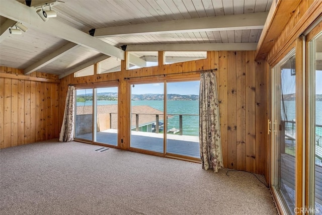 carpeted spare room with wood walls, lofted ceiling with beams, and a water view