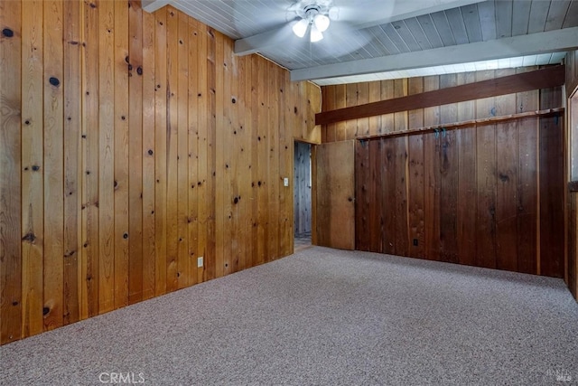 carpeted empty room featuring lofted ceiling with beams, ceiling fan, wooden ceiling, and wood walls