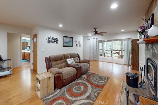 living room featuring a tiled fireplace, ceiling fan, and light hardwood / wood-style flooring