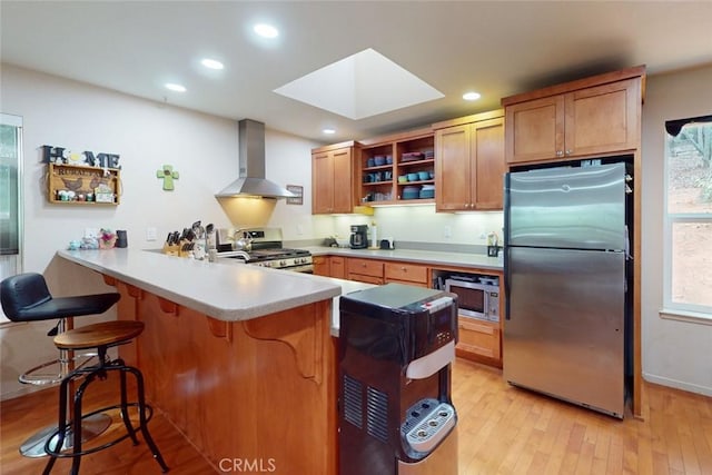 kitchen with wall chimney exhaust hood, stainless steel appliances, kitchen peninsula, light hardwood / wood-style floors, and a kitchen bar