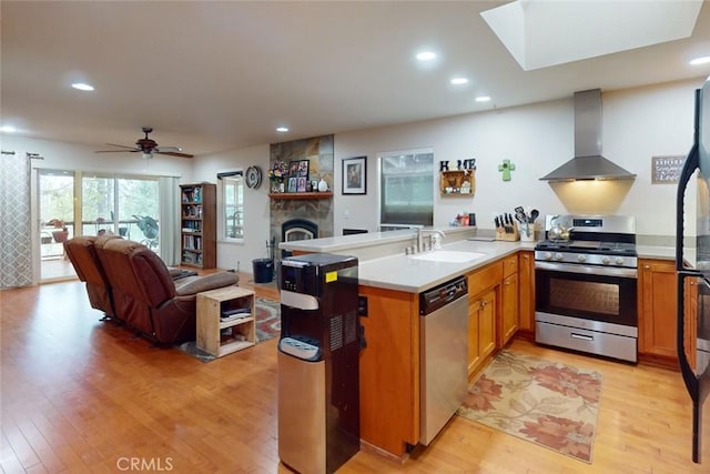 kitchen with ceiling fan, sink, stainless steel appliances, wall chimney range hood, and light hardwood / wood-style flooring