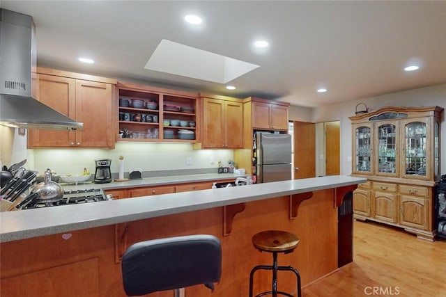 kitchen featuring a breakfast bar, a skylight, wall chimney exhaust hood, light hardwood / wood-style floors, and stainless steel appliances