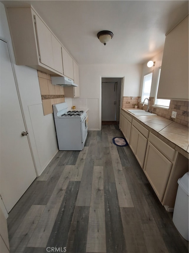 kitchen with tile counters, white gas range oven, wood-type flooring, backsplash, and sink