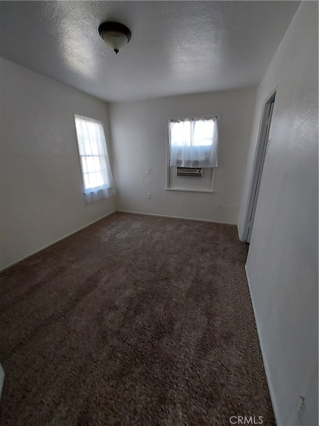 spare room featuring a healthy amount of sunlight, a textured ceiling, and dark colored carpet