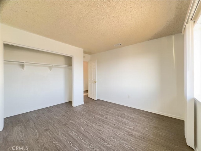 unfurnished bedroom with a textured ceiling, dark hardwood / wood-style flooring, and a closet