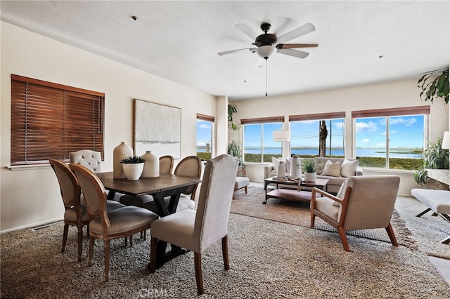 dining space with carpet flooring, ceiling fan, a water view, and a textured ceiling