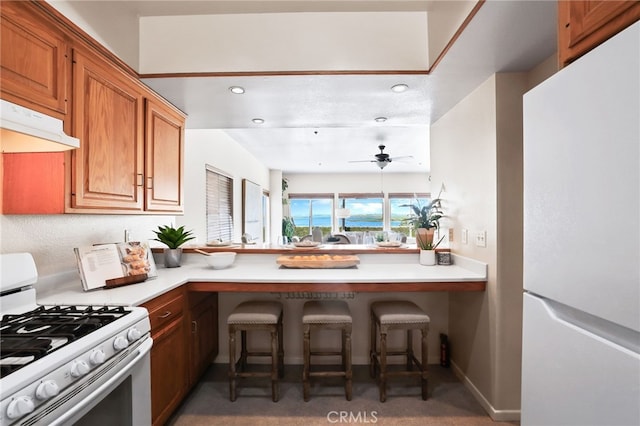 kitchen with a breakfast bar area, ceiling fan, and white appliances