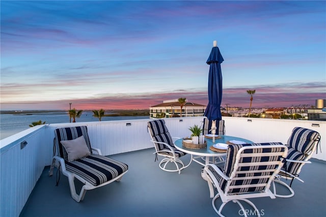 patio terrace at dusk featuring a water view and a balcony