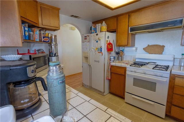 kitchen with tile countertops, ventilation hood, and white appliances