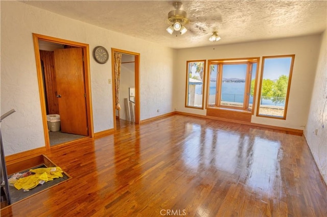 empty room featuring ceiling fan, hardwood / wood-style floors, a water view, and a textured ceiling