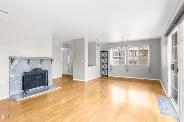 unfurnished living room featuring wood-type flooring, an inviting chandelier, and a stone fireplace