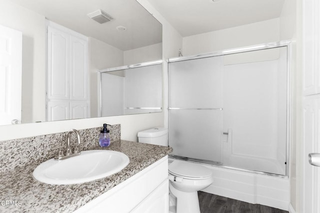 full bathroom with hardwood / wood-style flooring, vanity, toilet, and combined bath / shower with glass door