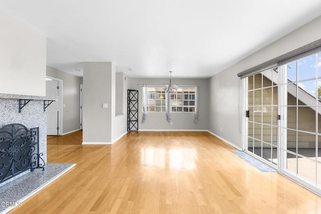 unfurnished living room with a tiled fireplace, light hardwood / wood-style flooring, and an inviting chandelier