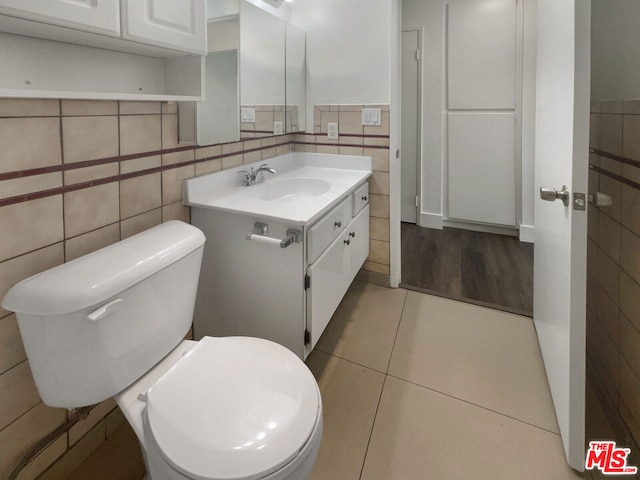 bathroom featuring tile patterned flooring, vanity, toilet, and tile walls