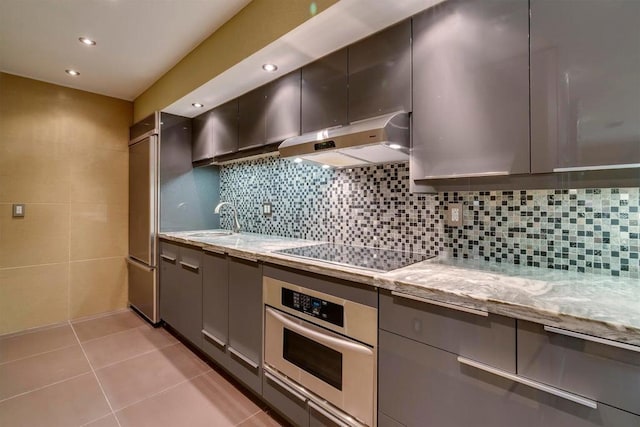 kitchen with stainless steel oven, sink, decorative backsplash, black electric cooktop, and light stone counters