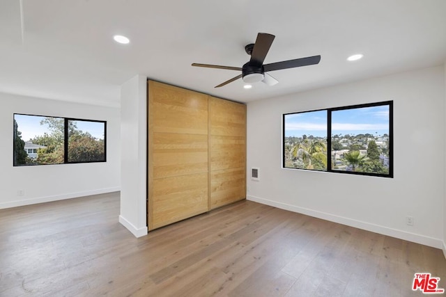 unfurnished bedroom featuring hardwood / wood-style floors, a closet, ceiling fan, and multiple windows