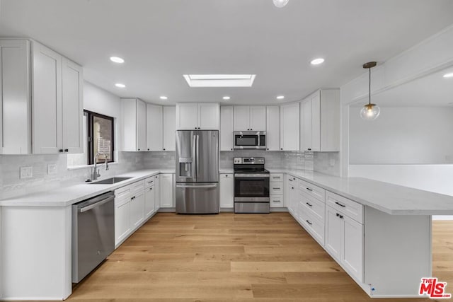 kitchen featuring light hardwood / wood-style flooring, a skylight, kitchen peninsula, appliances with stainless steel finishes, and sink