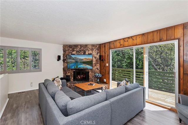 living room featuring plenty of natural light, a stone fireplace, wood-type flooring, and wooden walls