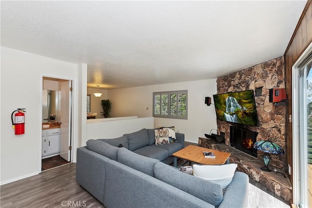 living room with a textured ceiling, dark hardwood / wood-style flooring, and a stone fireplace