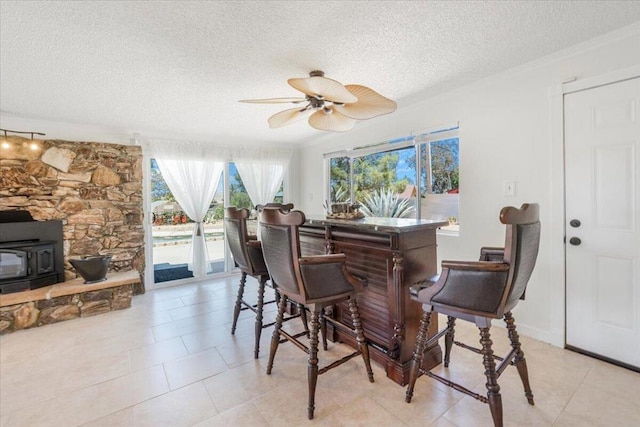 tiled dining space with ceiling fan, a textured ceiling, and a wood stove