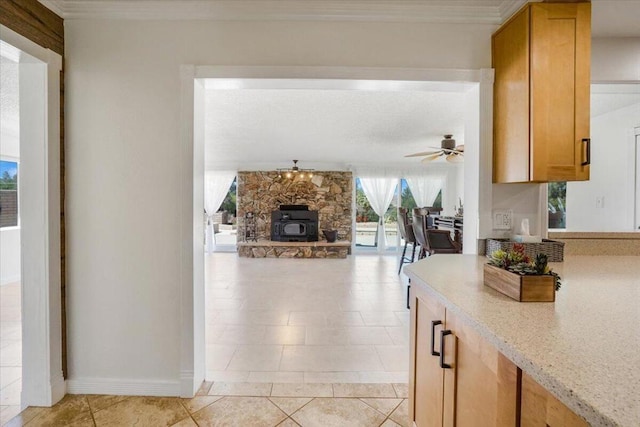 kitchen with ceiling fan, a stone fireplace, light stone counters, and light tile patterned floors