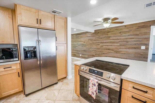 kitchen with light brown cabinetry, wooden walls, ceiling fan, and appliances with stainless steel finishes